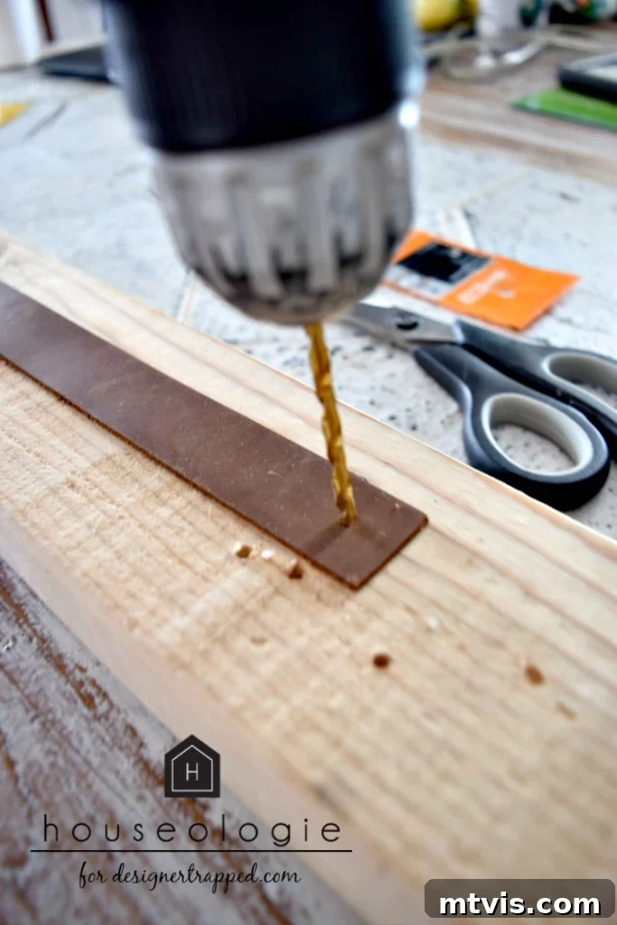 Action shot of a drill and drill bit being expertly used to create a precise hole in a strip of brown leather, preparing it for DIY drawer pull assembly.