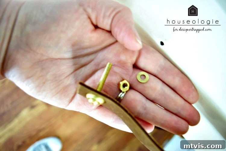 Detailed photo showing a woman's hand holding brass screws, nuts, and a strip of leather, illustrating the components used for DIY leather drawer pulls.