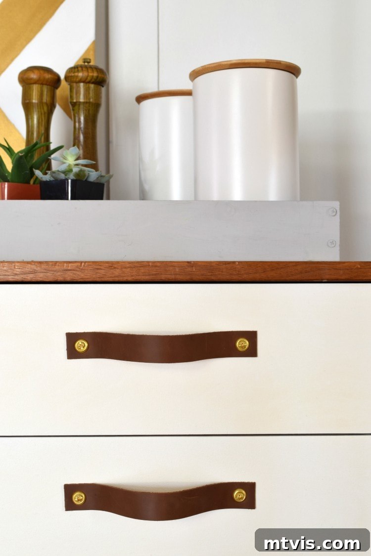 Close-up photo showcasing stylish leather drawer pulls with brass screws against modern white drawer fronts, highlighting the finished DIY look.