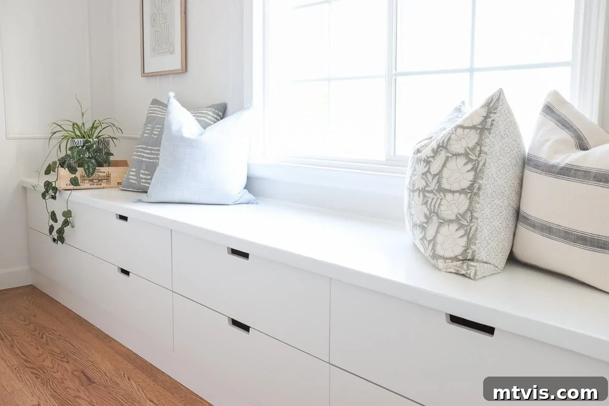 50 IKEA Hacks You Won't Believe Are IKEA 28 A charming white window seat, cleverly fashioned from IKEA Nordli drawers, extends along the living room wall beneath a sunlit window. Adorned with plush pillows and a vibrant plant, this long bench conceals generous storage drawers below, embodying a perfect blend of comfort and functionality.