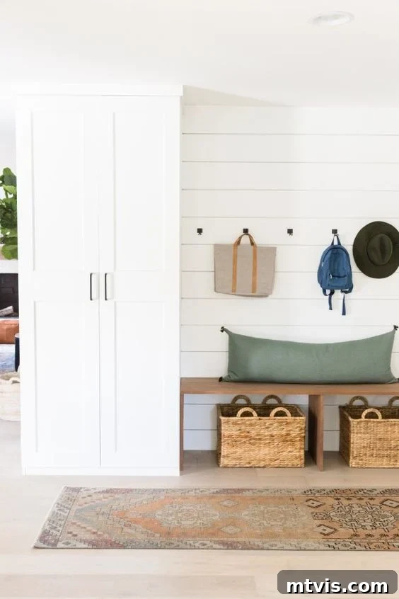 50 IKEA Hacks You Won't Believe Are IKEA 33 A meticulously designed mudroom setup along the outer wall of a house, skillfully crafted using DIY IKEA hacks. It features a custom Pax high cabinet with drawers and an integrated bench with practical storage underneath. Bags and hats are neatly hung on hooks above the clean, bare bench, creating an organized and inviting entryway.