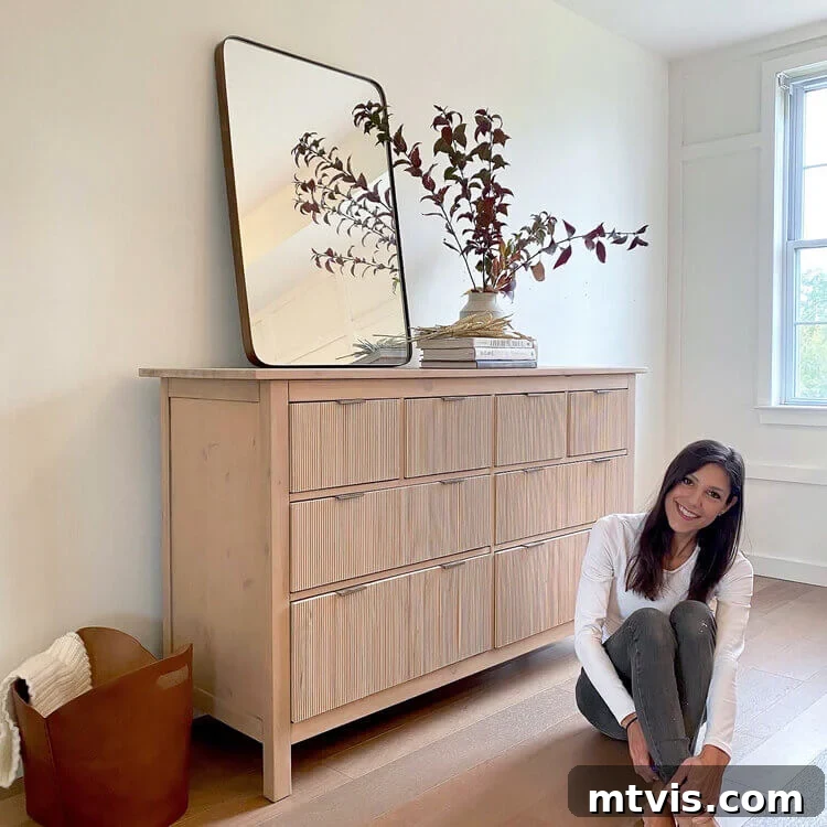 50 IKEA Hacks You Won't Believe Are IKEA 3 A smiling woman sitting on a wooden floor beside a beautifully transformed fluted Hemnes dresser, showcasing the successful outcome of a DIY IKEA hack. The dresser's unique texture adds a touch of sophistication to the room.