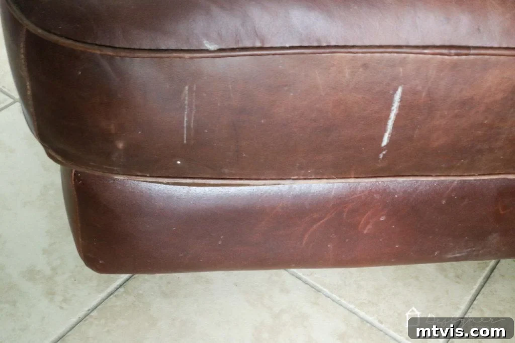Close-up of the damaged leather surface before restoration, showing paint marks and severe wear.