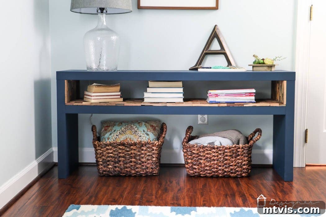 Upgrade Your IKEA Lack Designer Style Without the Price Tag 2 A blue-painted IKEA lack hack created this short table with a shelf by a door that has storage for books. baskets, and a surface for a lamp and a large letter "A." The "designertrapped.com" logo is in the lower right corner.