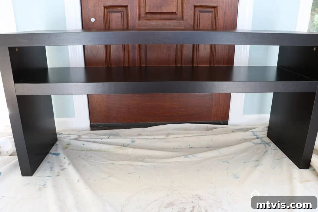 Upgrade Your IKEA Lack Designer Style Without the Price Tag 3 A black IKEA Lack sofa table on a painter's drop cloth in front of a brown door.