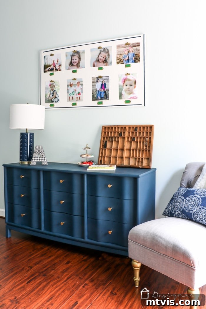 A beautifully painted blue dresser with gold knobs stands next to a comfortable gray tufted armchair. Its top surface is elegantly styled with various decor and books, while a large photo collage of children hangs on the wall above. This piece showcases a successful furniture painting project using proper techniques.