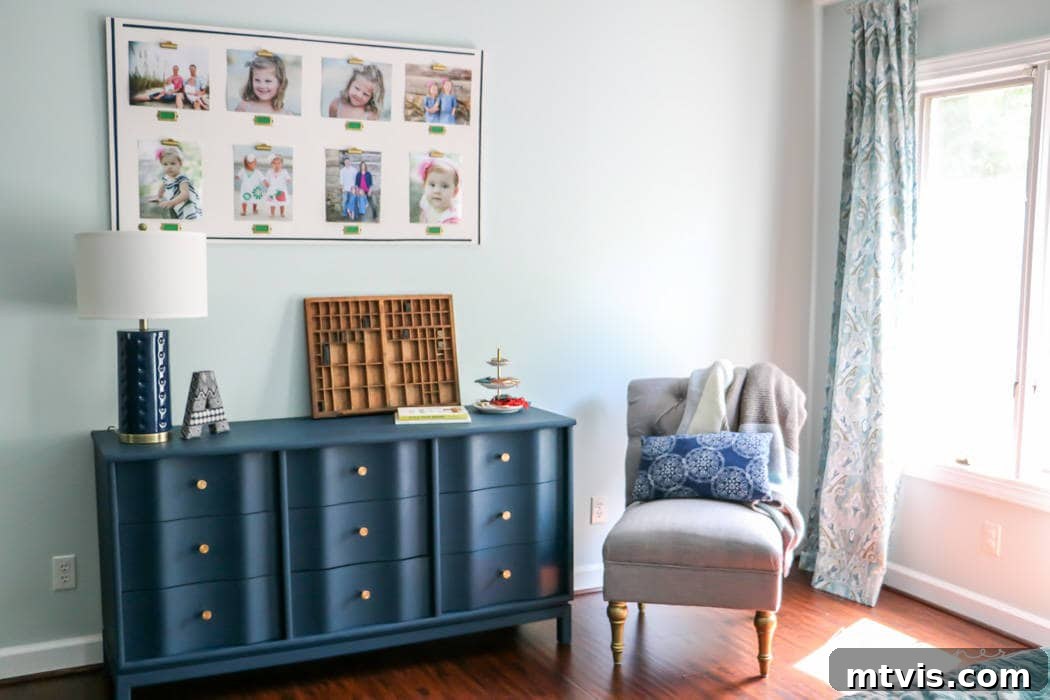 A bright room corner features a painted blue wood dresser with gold knobs, tastefully styled with books and decor, positioned next to a gray chair by a sunlit window. A heartwarming collage of children's photos hangs prominently above, illustrating how painting wood furniture can enhance and personalize a family living space.