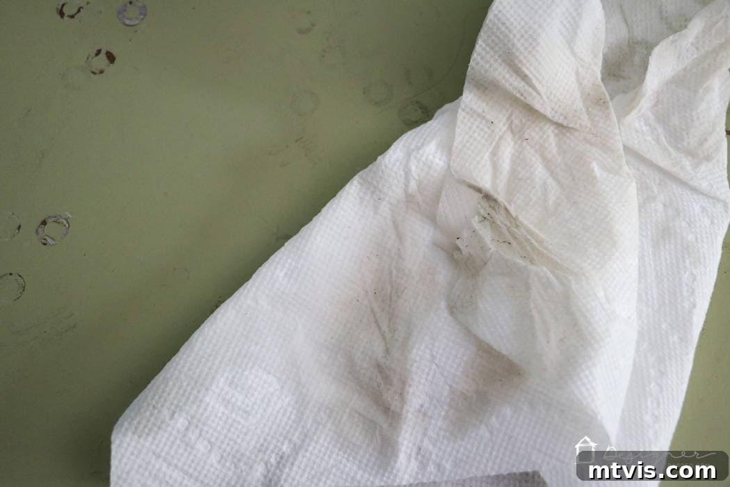 A paper towel heavily soiled with residue and dirt rests on a dull green surface, serving as visible proof of the effectiveness of Simple Green cleaner and emphasizing its crucial role in preparing wood furniture for painting.
