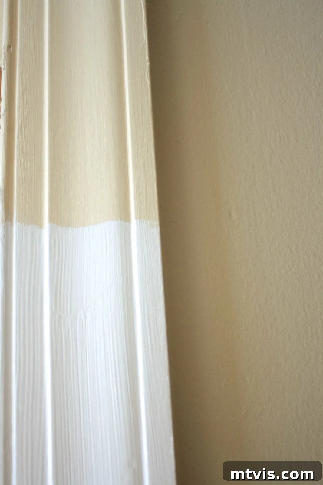 DIY Drama Black Doors White Trim 3 A close-up of door trim, half painted pale beige and the bottom half painted with a new coat of bright white paint.