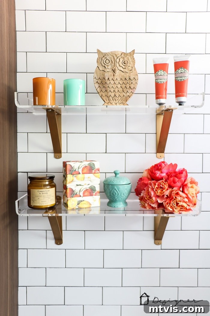 The floor-to-ceiling subway tile in this DIY bathroom remodel provides a stunning backdrop for modern lucite shelves, demonstrating elegant design on a budget.