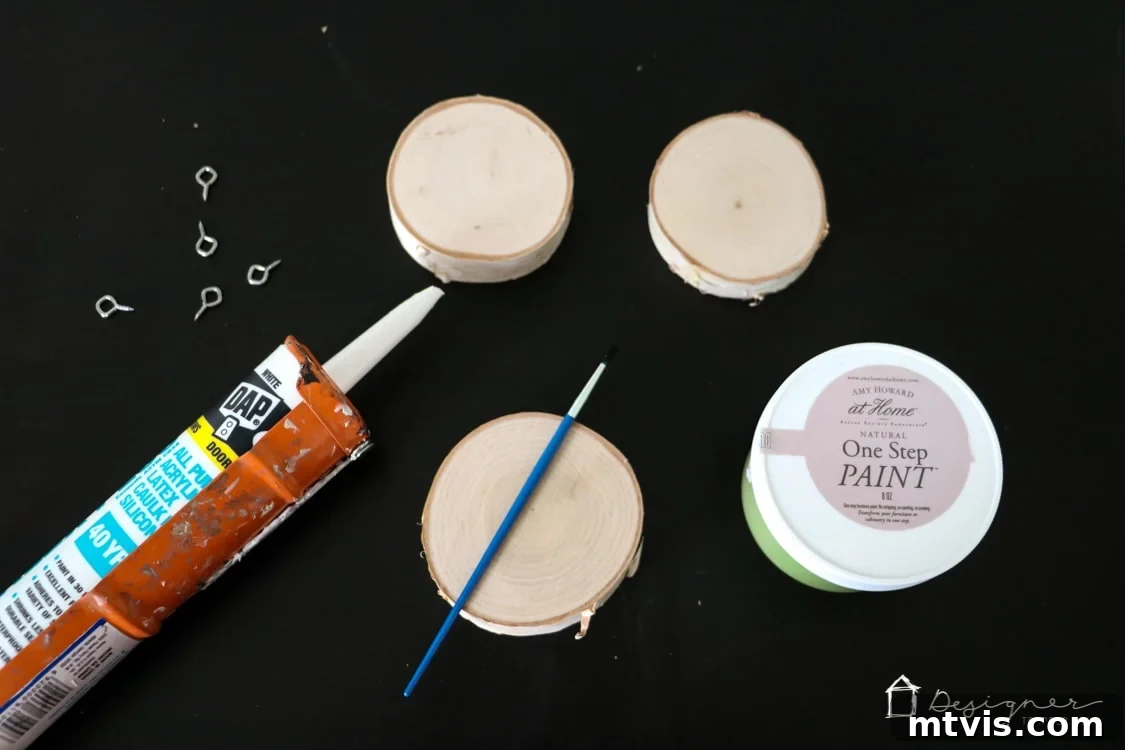 Create Stunning Textured Holiday Decor 3 Gathered materials for crafting textured Christmas ornaments, including a wood slice, caulk tube, caulk gun, paint, and brushes.