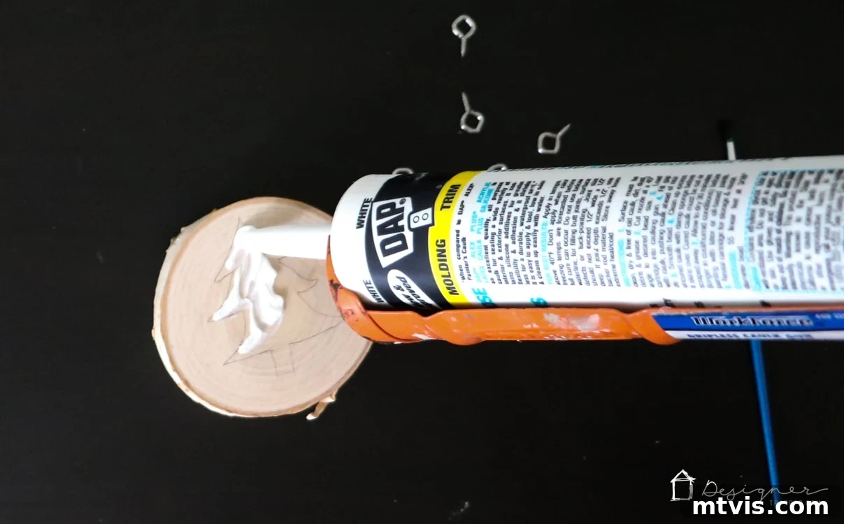 Create Stunning Textured Holiday Decor 5 Applying caulk along the pencil outline of a Christmas tree on a wood slice using a caulk gun.