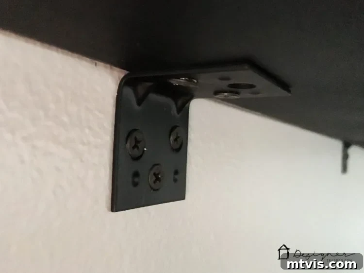 Securely fastening the underside of the DIY pipe desk to the wall using an angle bracket for added stability.