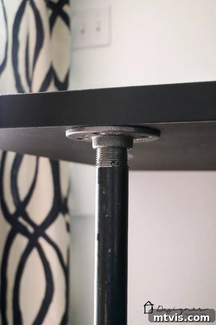 Close-up shot of the industrial pipe leg and floor flange connection, highlighting the robust assembly of the DIY desk.