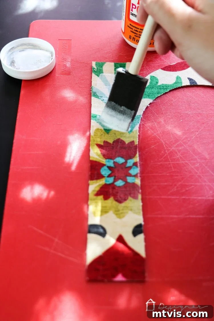 Applying final Mod Podge coat to fabric letters to prevent fraying, then attaching them to the wall with double-sided poster tape.
