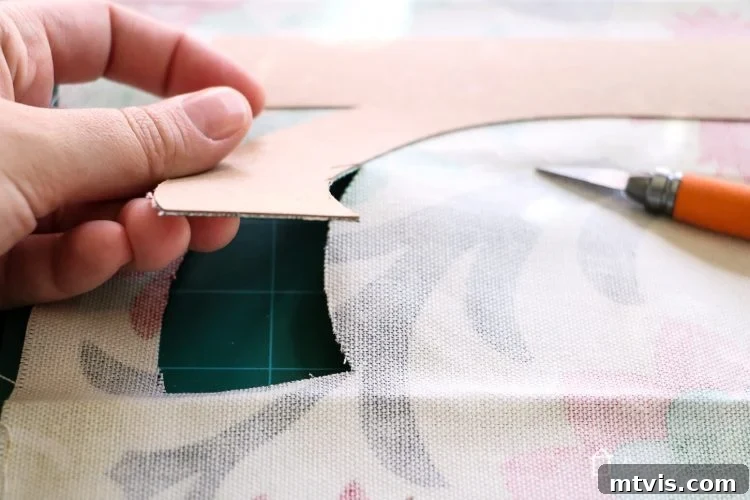 Using an exacto knife to precisely cut around fabric-covered chipboard letters for clean, professional edges.