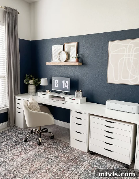Smart IKEA Desk Upgrades on a Budget 14 A meticulously arranged IKEA desk setup for an office and craft room, boasting a long white countertop and numerous drawers underneath. The space is highlighted by a vibrant blue color block wall and dedicated area for a Cricut machine, showcasing thoughtful organization.