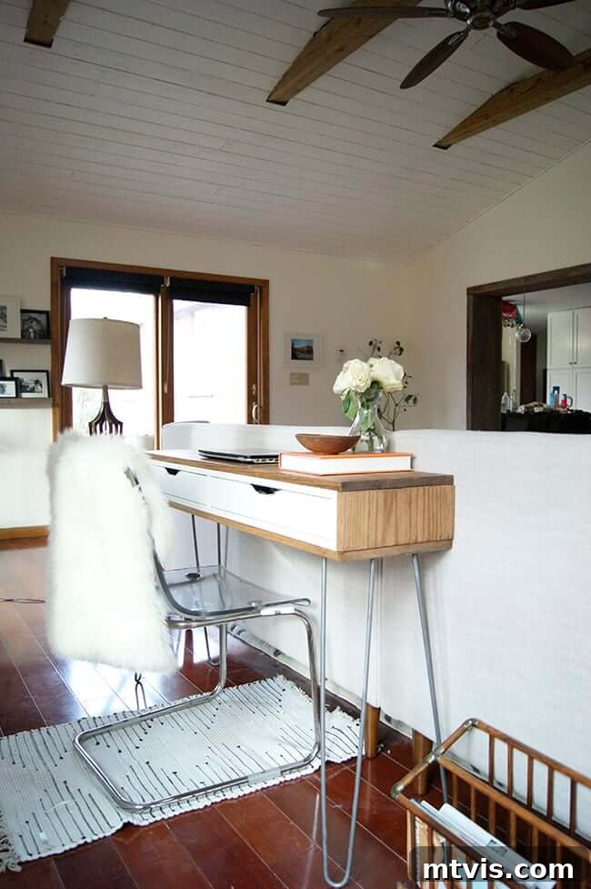 Smart IKEA Desk Upgrades on a Budget 9 A spacious living room featuring a minimalist slim IKEA desk positioned behind a white couch. High ceilings and a ceiling fan enhance the room's airy, minimalist aesthetic, complemented by this understated IKEA desk hack.