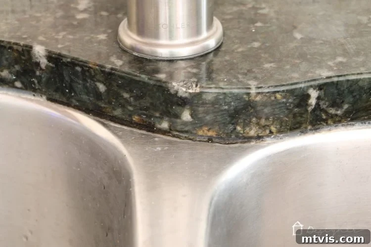 Close-up of severely discolored and moldy caulk around a kitchen sink, highlighting the need for replacement. Before caulk replacement.