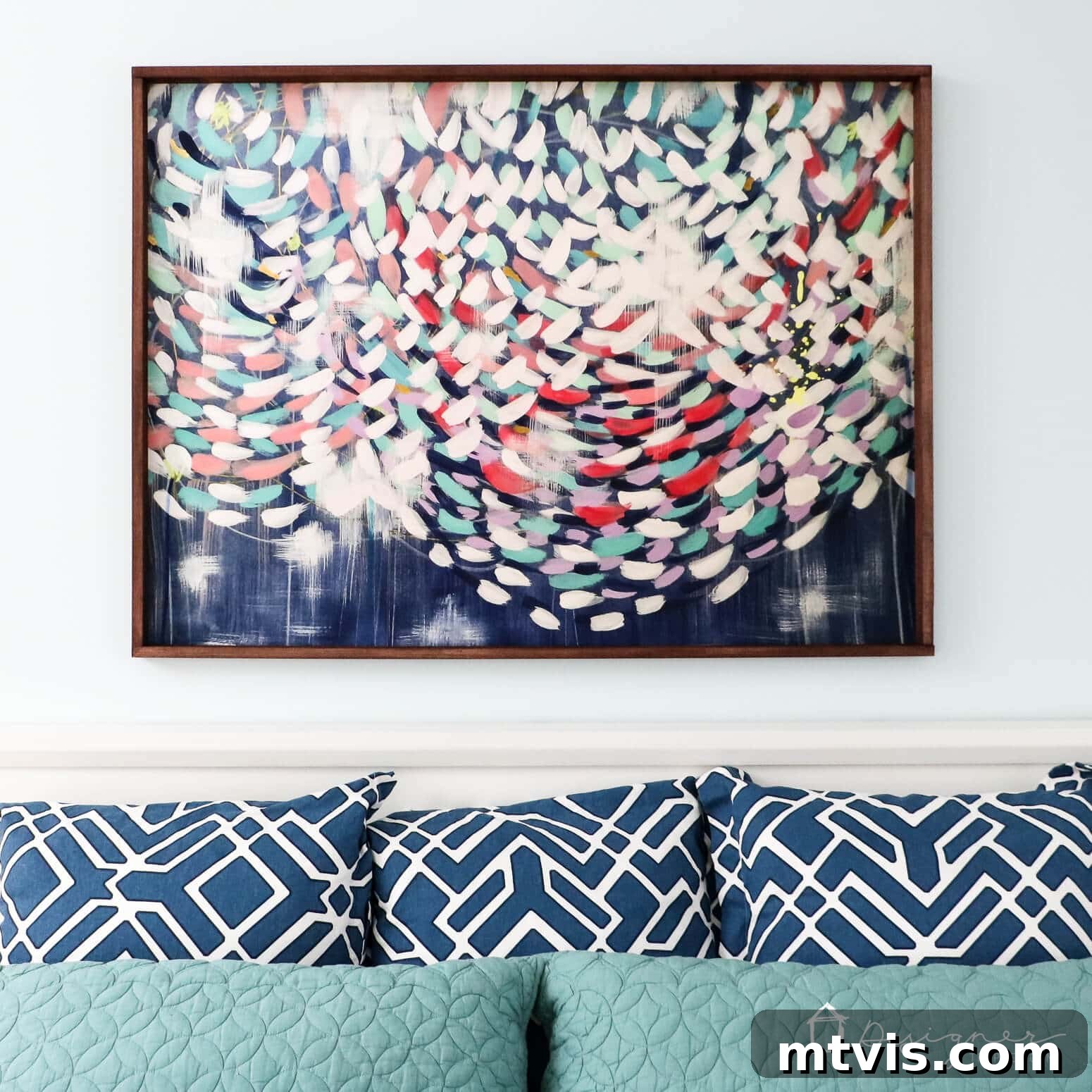 Build Custom Frames for Your Oversized Art 10 A vibrant, colorful abstract art print is elegantly housed in a thin, dark wood DIY frame, positioned above a stylish teal headboard with soft blue pillows, showcasing a finished project from the 'how to make a picture frame' tutorial.
