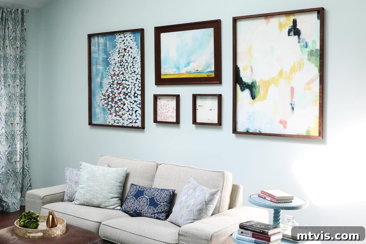 Build Custom Frames for Your Oversized Art 15 A beautifully curated gallery wall showcases six abstract art pieces of various sizes, each framed in dark wood following the detailed 'How to Make a Picture Frame' tutorial. This impressive display hangs above a comfortable cream-colored couch, complemented by blue and white throw pillows.