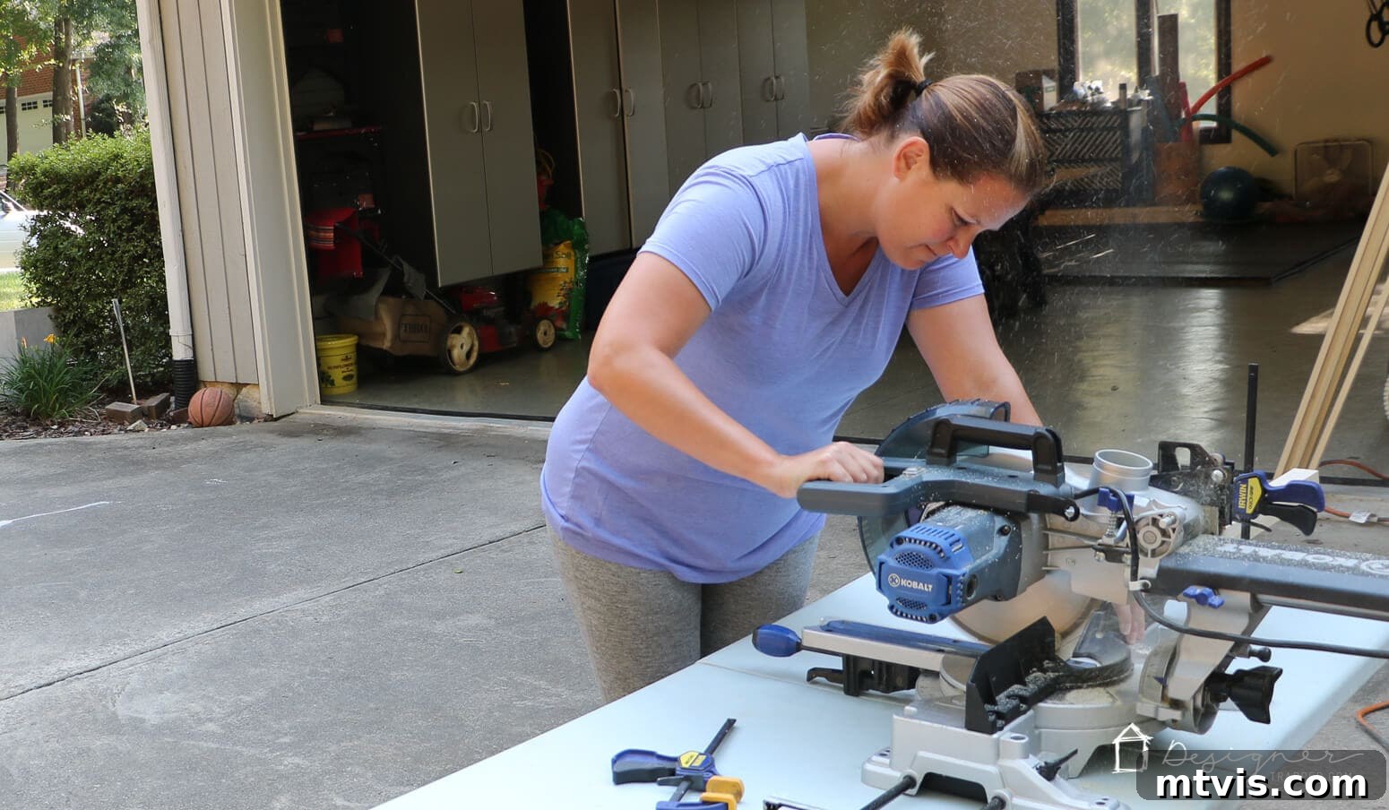 Build Custom Frames for Your Oversized Art 3 Tasha demonstrates how to make a picture frame by using a compound miter saw to precisely cut pine boards in her driveway, ensuring accurate dimensions for the DIY art frames.