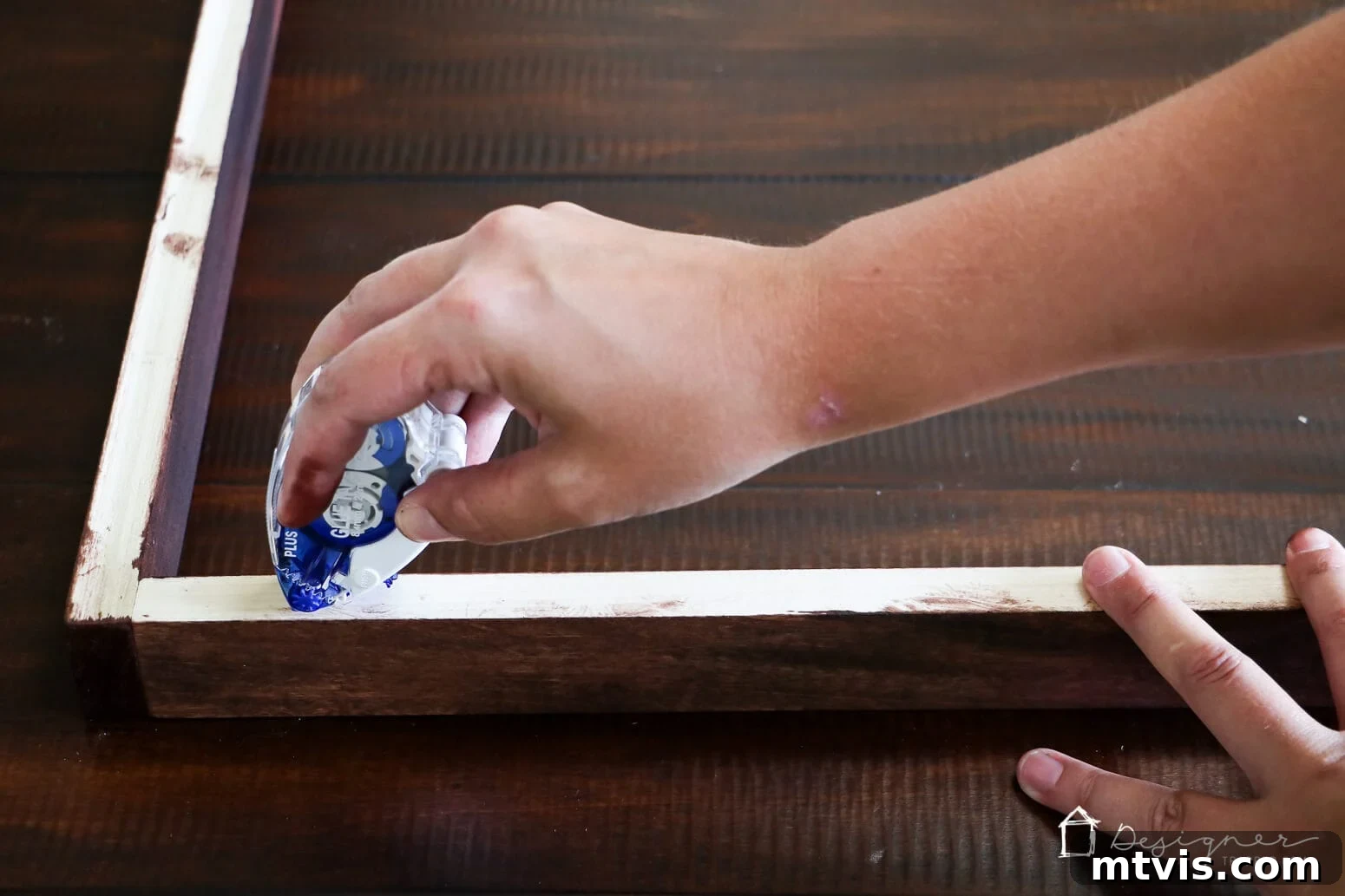 Build Custom Frames for Your Oversized Art 8 Tasha's hand deftly applies glue tape to the back inner edge of a large, stained DIY art frame, preparing it to secure a print. This step is crucial for mounting artwork in a homemade picture frame.