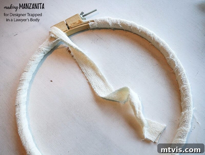 Craft Your Boho Winter Wreath 4 Begin your DIY Boho Winter Wreath by wrapping the embroidery hoop with soft, ripped white fabric strips. Secure the fabric and cover the entire hoop, including the tightening screw, for a cohesive and rustic base.