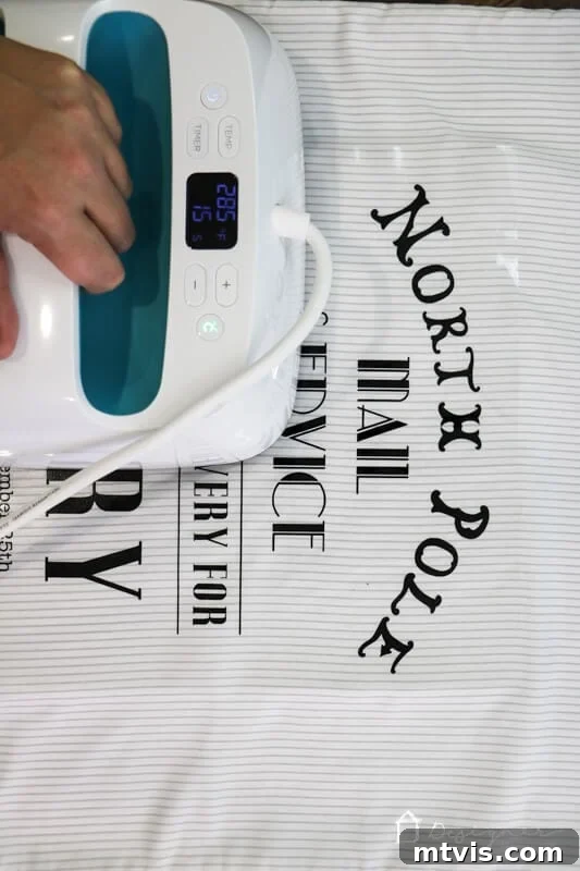 Handcrafted Santa Sacks for Magical Christmas Mornings 5 A person using a Cricut EasyPress to apply heat transfer vinyl onto a DIY Santa sack, demonstrating the precise application process