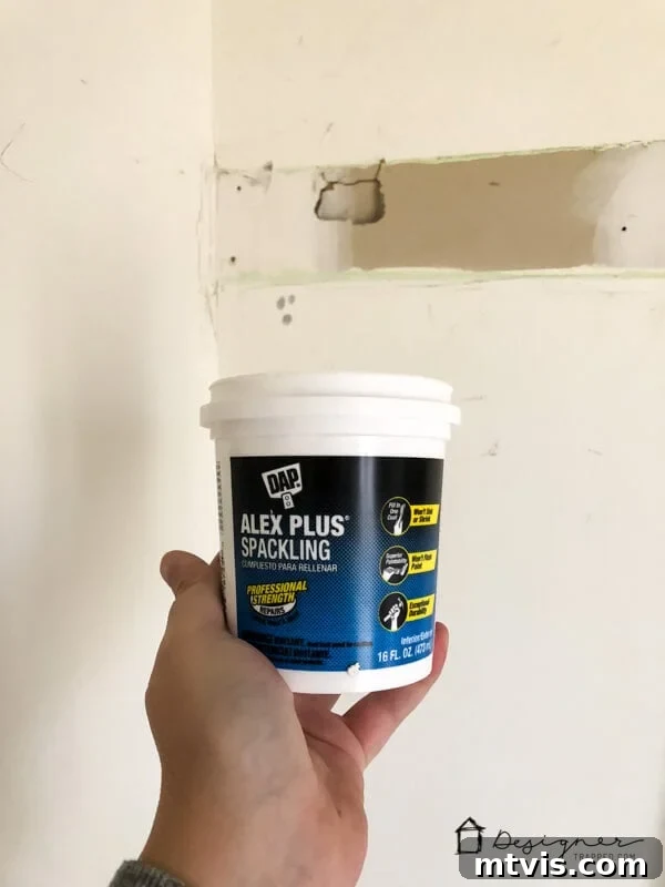 How to Repair Drywall: Tips for Minor Repairs 6 Alex Plus Spackling Paste being held up in front of damaged drywall