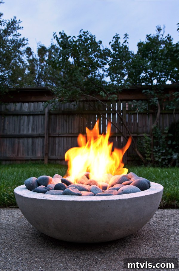 From Cozy Corners to Grand Gatherings: Fire Pit Ideas for All Spaces 5 A sleek DIY concrete bowl fire pit rests on a bed of gravel in a well-maintained backyard, framed by a classic wooden fence, exuding modern simplicity.