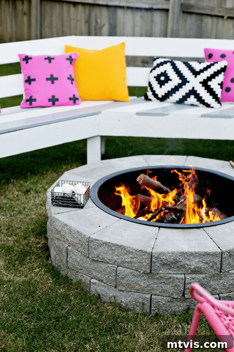 From Cozy Corners to Grand Gatherings: Fire Pit Ideas for All Spaces 8 Among the best fire pit ideas is this easy DIY fire pit, constructed from landscaping stones, elegantly circled by white benches adorned with cheerful yellow, pink, and black and white pillows, creating a cozy and inviting outdoor gathering space.
