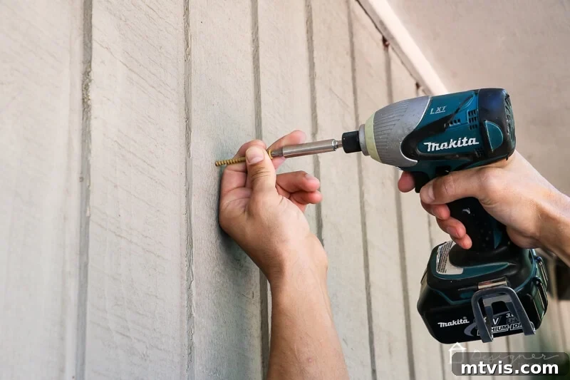 Installing the outdoor chalkboard onto a cedar-sided house with a deck screw.