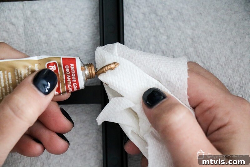 Applying Rub N Buff to a black plastic frame, showing the immediate transformation to a rich gold finish.