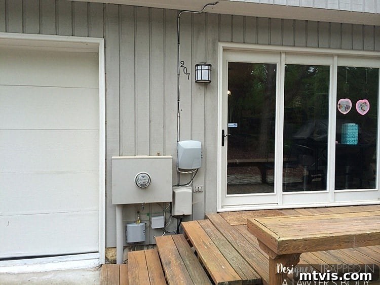 Before image showing a prominent cluster of utility boxes attached to the side of a contemporary house, near the back door.