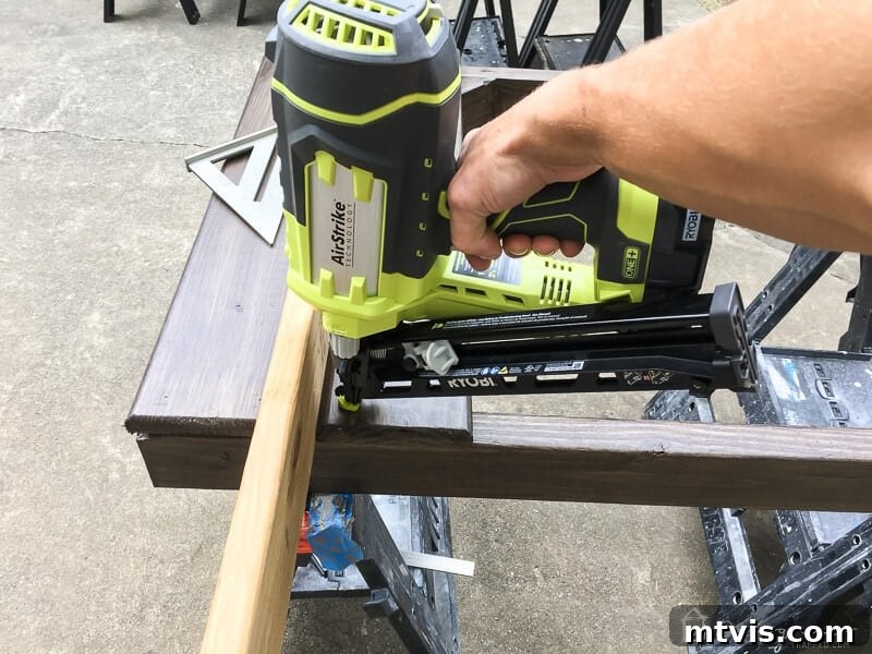 Person using a nail gun to attach horizontal wooden slats to an outdoor gate door frame, with a spacer in place.