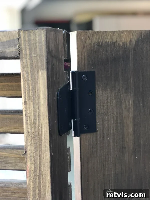 Close-up of a heavy-duty gate hinge installed on the wooden outdoor electrical box cover, highlighting the access mechanism.