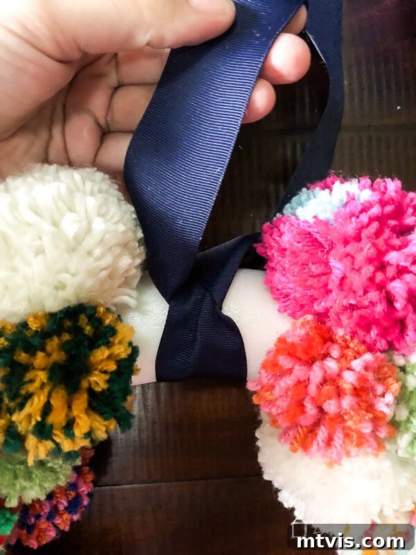 Fluffy Pom Pom Wreath Craft 8 Tying navy blue ribbon onto a DIY pom pom wreath for hanging