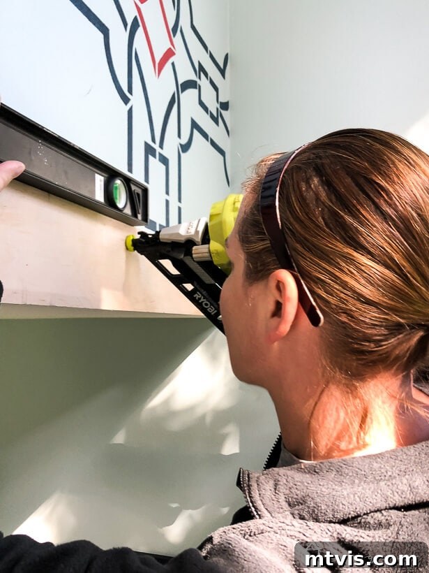 Attaching a wood plank to the wall using a finish nail gun, demonstrating proper technique.