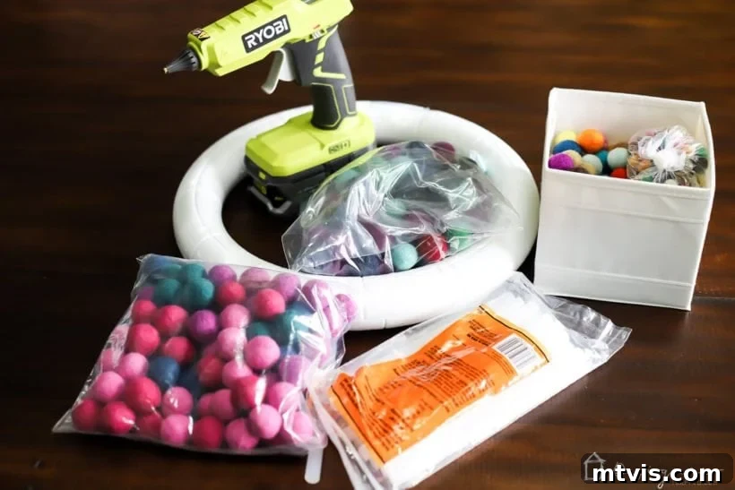 Vibrant Felt Ball Wreath Project 3 Essential supplies for crafting a DIY felt ball wreath laid out on a clean surface, including colorful felt balls, a foam wreath form, hot glue gun, and ribbon.