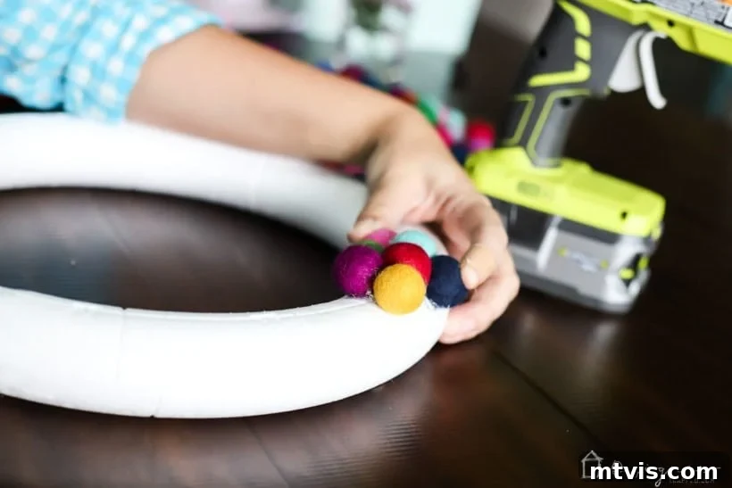 Vibrant Felt Ball Wreath Project 5 Another perspective of a woman diligently hot-gluing colorful felt balls onto a wreath form, showing the steady progression of the DIY felt ball wreath.