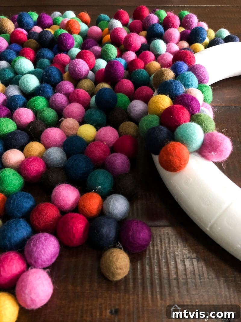 Vibrant Felt Ball Wreath Project 6 A partially covered colorful DIY felt ball wreath, showing the progress of felt balls meticulously glued onto the foam base, highlighting the vibrant color palette.