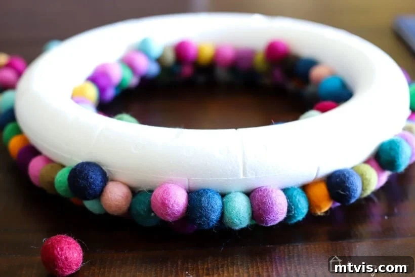 Vibrant Felt Ball Wreath Project 7 Close-up image of a DIY felt ball wreath being crafted, with colorful felt balls densely packed around the sides and edges of the wreath form.