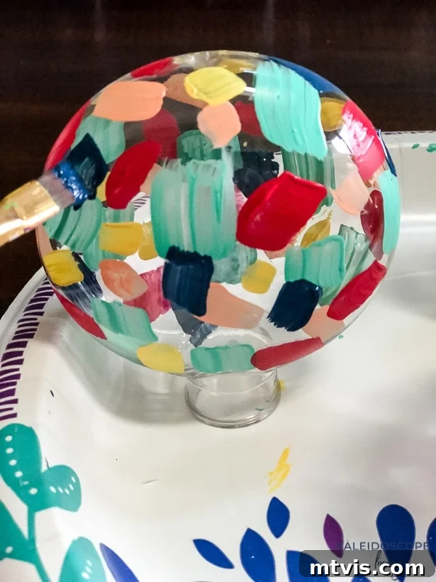 Craft Your Own Hand-Painted Christmas Ornaments 6 Process of painting a plastic ornament, showing layers of colorful brushstrokes being applied.