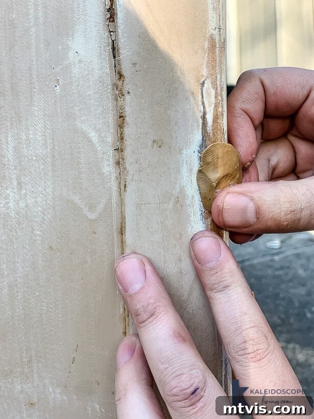 A close-up of hands filling in the damaged spot wit epoxy wood filler putty as sun shines above the work. 
