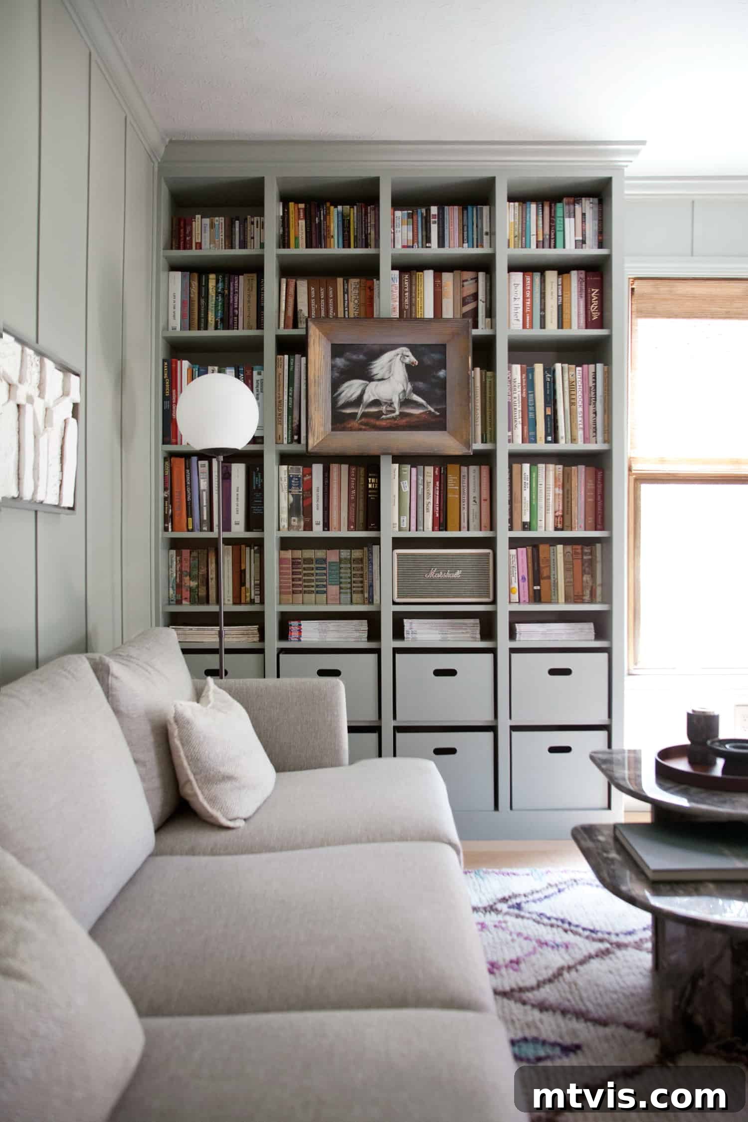 IKEA Smart Hacks: Custom Built-Ins and Bookshelf Upgrades 9 IKEA built-in cabinets in a home library hold floor to ceiling books with a row of cubby boxes on the lower two shelves. A gray couch rests again the connecting wall.