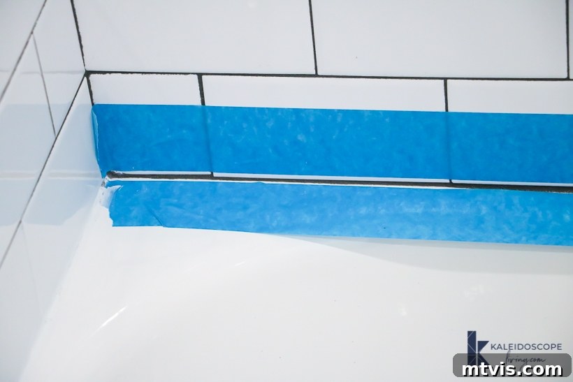 Caulking Made Easy A Beginner's Guide 5 A close-up of two strips of blue painter's tape on white tiles, prepping tub for caulking.