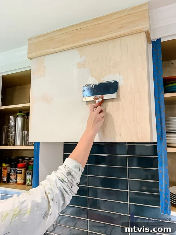 Wood and White Concrete: A DIY Range Hood Transformation 8 Applying the first thin layer of white skimcoat concrete to the range hood frame using a drywall knife
