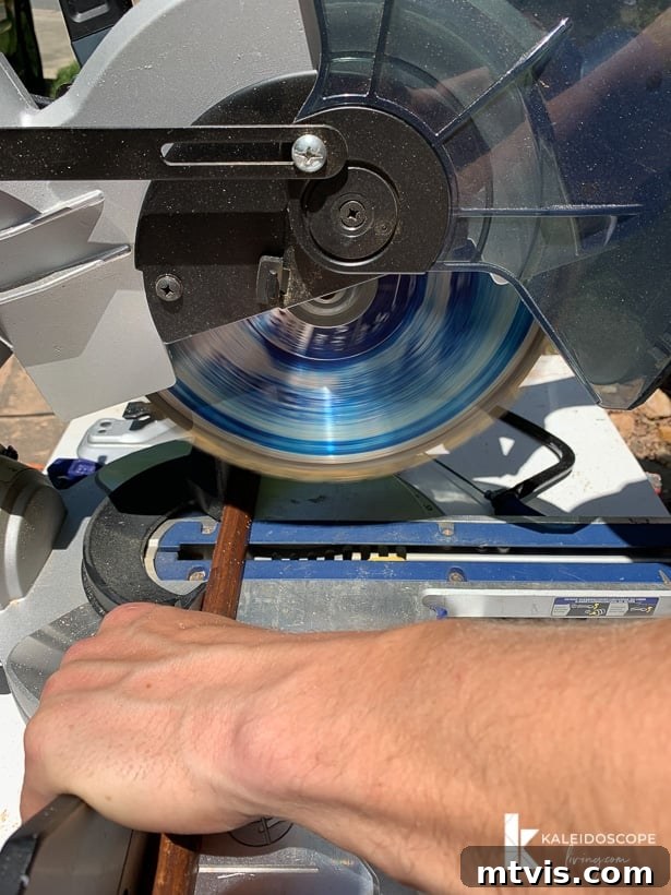 DIY Quarter Round Molding Installation 4 A man is cutting quarter round molding trim with a compound miter saw. The corner text reads, 'KaleidoscopeLiving.com.'