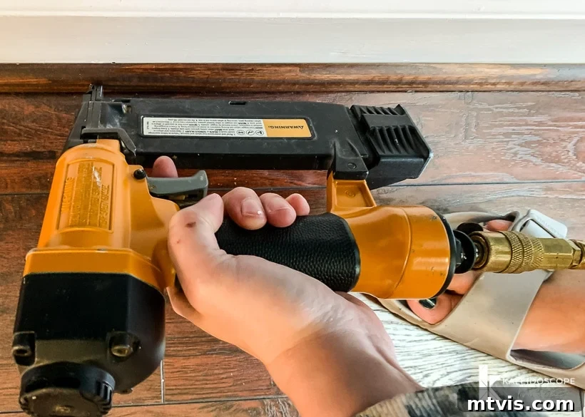 DIY Quarter Round Molding Installation 6 A hand is using a brad nailer to install quarter round molding, securing it to the wall and floor.